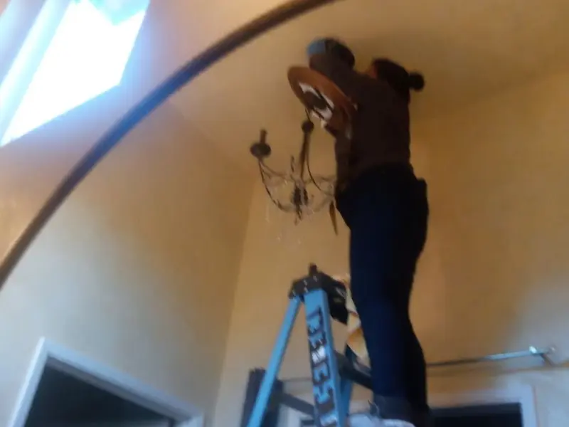 Electrician installing a chandelier in a Mena residence
